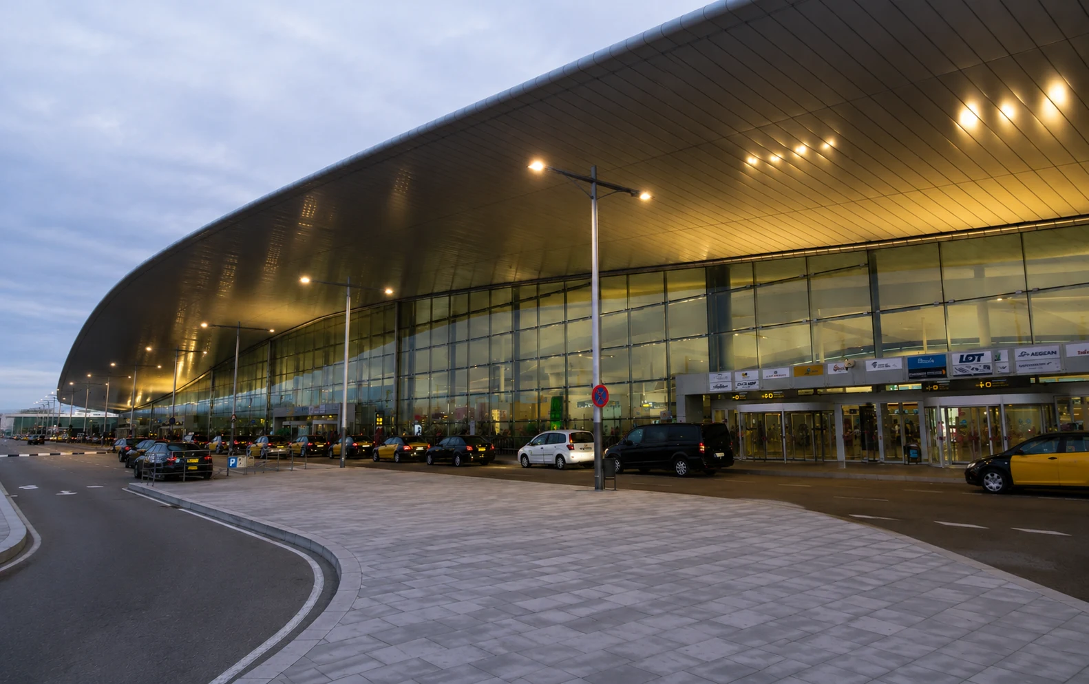 Barcelona Airport Terminal 1 exterior with modern glass facade, taxi pickup area, and passenger drop-off zone in Spain